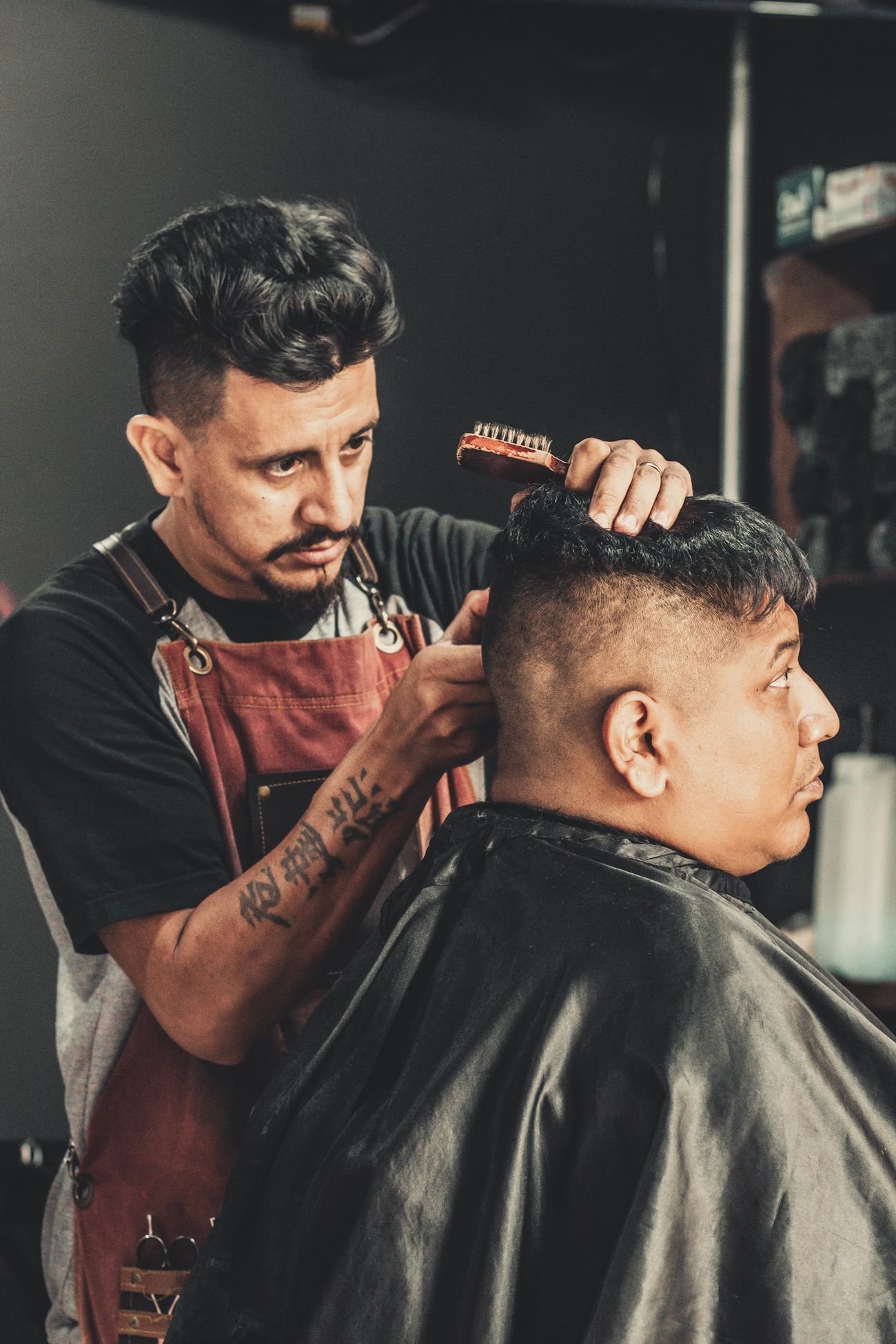 Un barbero de delantal peinando y cortando el cabello de un cliente
